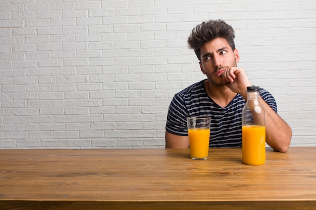 Homem considerável e natural novo que senta-se em uma tabela que duvida e confuso, pensando de uma ideia ou preocupado com algo.