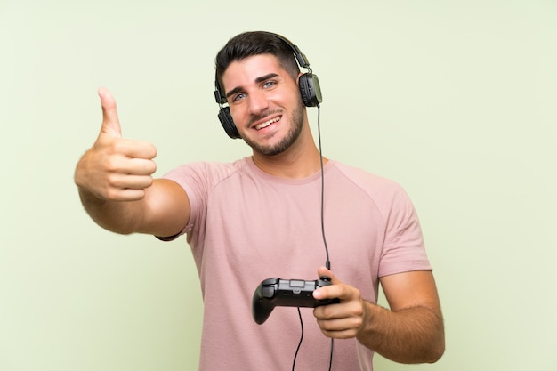 Homem considerável novo que joga com um controlador do jogo video sobre a parede verde isolada