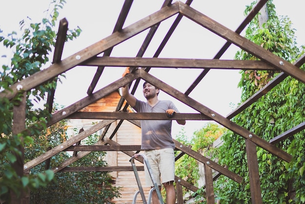 Homem construindo telhado de madeira ao ar livre em pé na escada