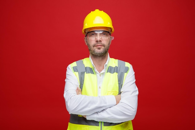 Homem construtor em uniforme de construção e capacete de segurança olhando para a câmera com expressão séria e confiante em cima de fundo rosa