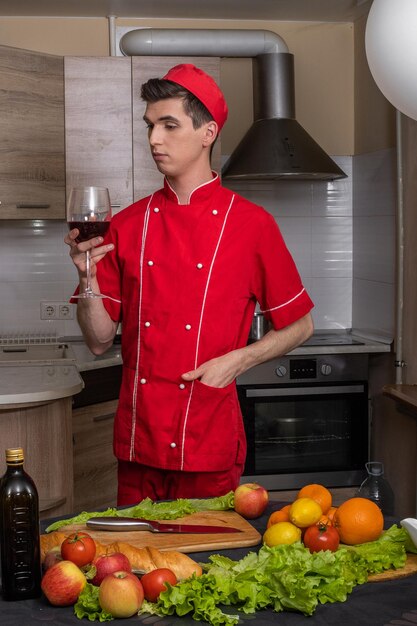 Homem Cook em uniforme vermelho degustando vinho na cozinha