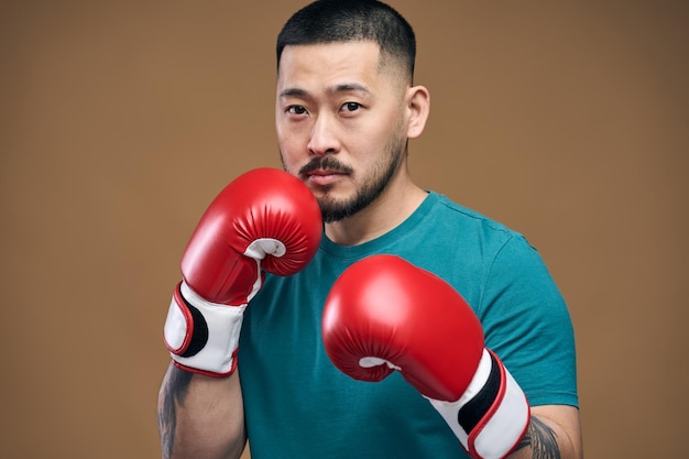 Homem coreano sério em camiseta verde usando luvas de boxe e olhando para a câmera