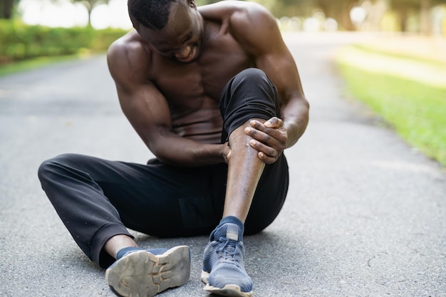 Foto homem corredor africano sentado na pista de corrida e sentindo dores na perna copie o espaço