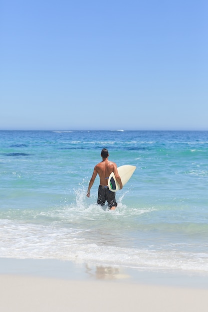 Homem correndo na praia com sua prancha de surf