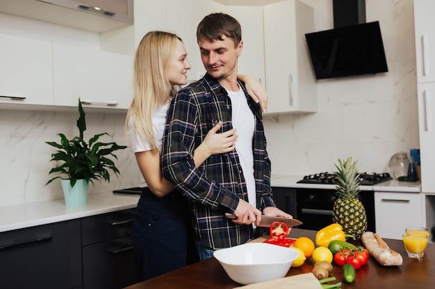 Homem corta pimenta enquanto sua esposa o abraça por trás