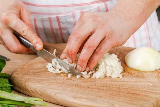 Homem corta uma cebola branca com uma faca O conceito de cozinhar