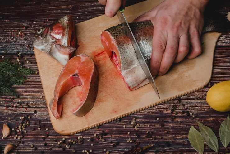 Foto homem corta uma truta com uma faca em uma placa. peixe cru fresco