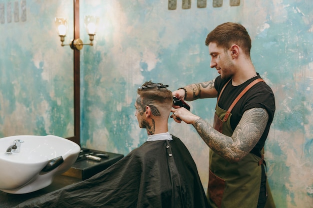 Homem cortando cabelo da moda na barbearia. o cabeleireiro masculino em tatuagens atendendo o cliente.