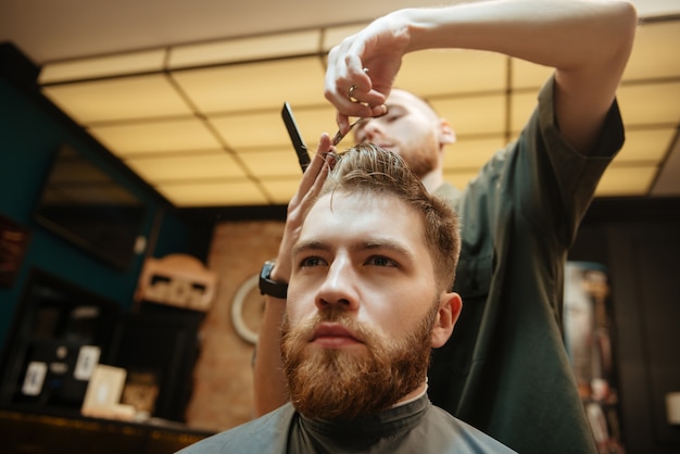 Homem cortando cabelo de cabeleireiro com uma tesoura enquanto está sentado na cadeira.