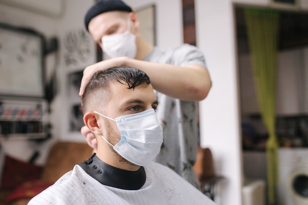 Homem cortando cabelo na barbearia usando máscara durante a pandemia de coronavírus. Barbeiro profissional usando luvas. Covid-19, conceito de beleza, autocuidado, estilo, saúde e medicina.