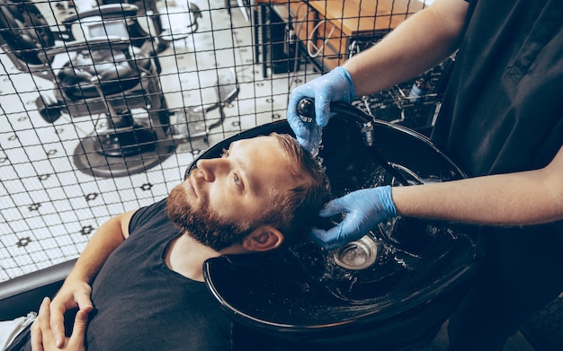 Homem cortando cabelo na barbearia usando máscara durante a pandemia de coronavírus. barbeiro profissional usando luvas. covid-19, conceito de beleza, autocuidado, estilo, saúde e medicina.