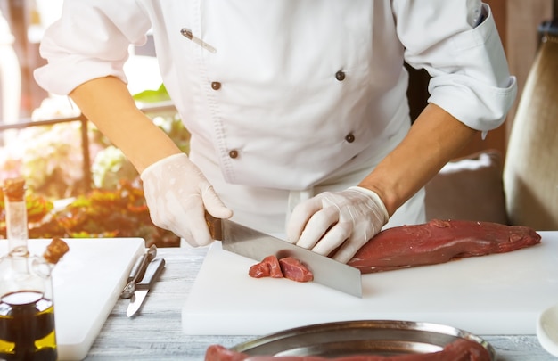 Homem cortando carne com carne de faca deitada na preparação de tábua de carne de vitela em restaurante de manhã ocupada ...