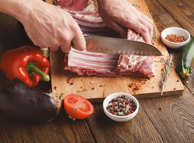 Homem cortando costela de cordeiro na placa de madeira na cozinha do restaurante. chef preparando carne fresca para cozinhar. cozinha moderna com espaço de cópia