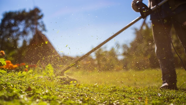 Homem cortando grama alta com aparador de grama elétrico ou a gasolina no quintal Ferramentas e equipamentos de cuidados de jardinagem Processo de corte de grama com cortador manual