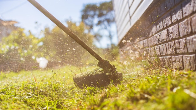 Homem cortando grama alta com aparador de grama elétrico ou a gasolina no quintal Ferramentas e equipamentos de jardinagem Processo de corte de grama com cortador manual