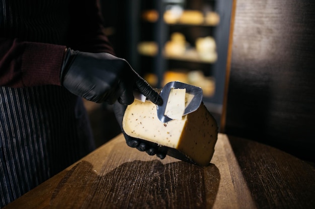 Homem cortando um pequeno pedaço de queijo para saborear Um jovem trabalhador usa uma faca especial para queijo