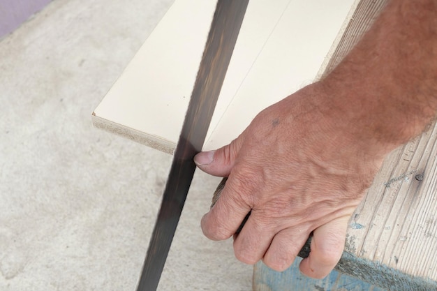 Homem cortando uma tábua de madeira com uma serra de mão no jardim