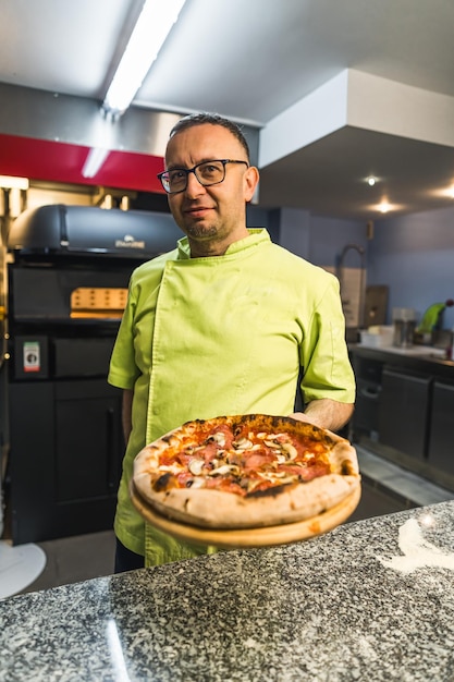 Homem cozinha com pizza na cozinha da padaria tiro vertical médio