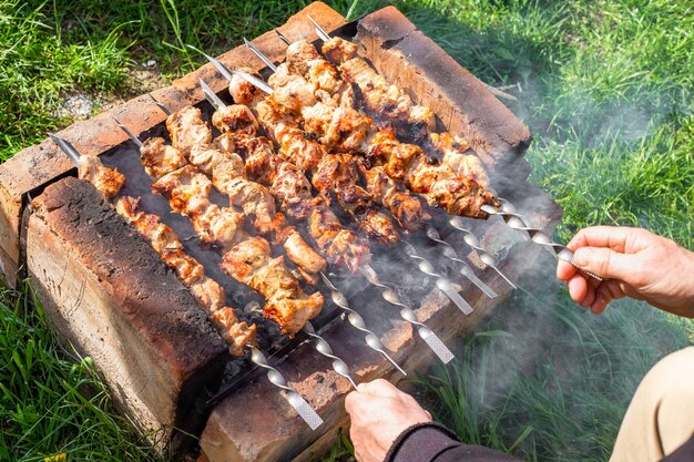 Homem cozinha um suculento kebab de carne em uma grelha caseira virando os espetos de piquenique de primavera fritos