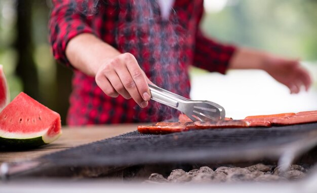 Homem cozinhando comida saborosa na churrasqueira para jantar francês ao ar livre perto do rio na bela noite de verão na natureza