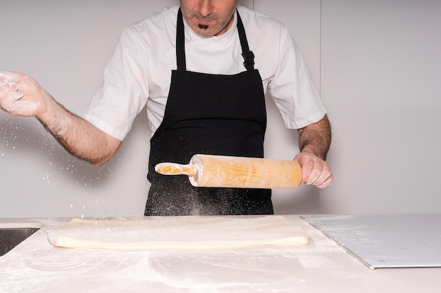 Homem cozinhando croissants caseiros preparando a massa folhada e adicionando farinha e achatando-a