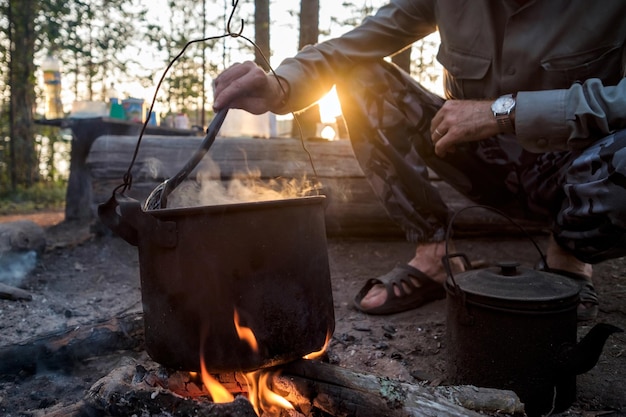 Homem cozinhando em bowlers sobre um incêndio na floresta