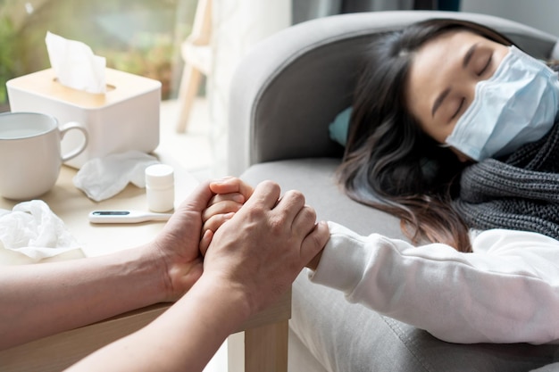 Foto homem cuidando da namorada sofrendo dor de doente deitado no sofá na sala de estar em casa marido segurando a mão da esposa sente-se com amor e cuidado em casa adorável ásia casal apoia juntos closeup