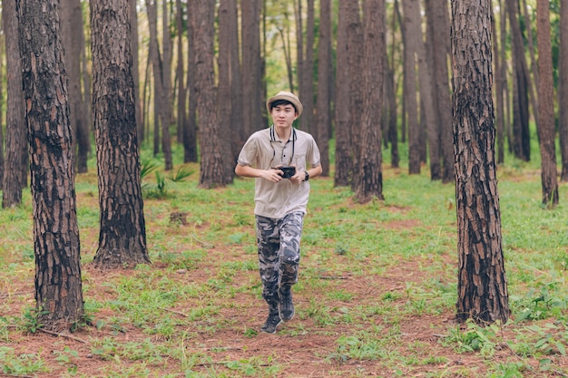 Homem da ásia usa camisa, chapéu e calças de camuflagem estão correndo e tirando fotos na floresta