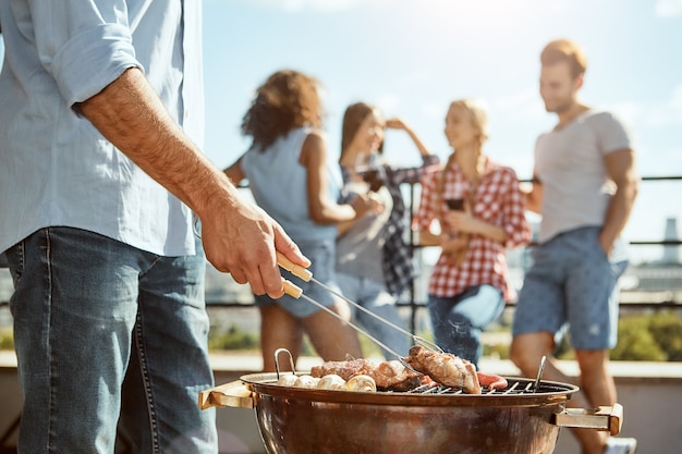 Homem da hora do churrasco fazendo churrasco de carne na grelha enquanto fica de pé no telhado com os amigos