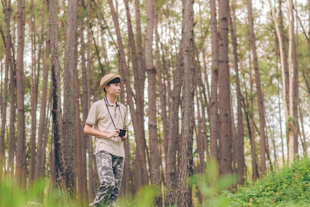 Homem da Ásia usa camisa, chapéu e calças de camuflagem estão andando e tirando fotos na floresta