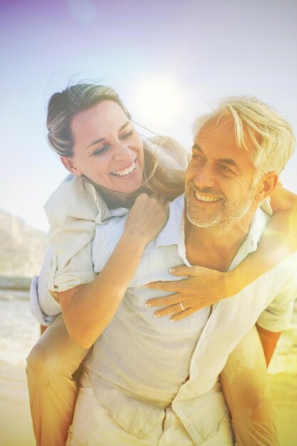 Foto homem dando carona para sua esposa sorridente na praia em um dia ensolarado