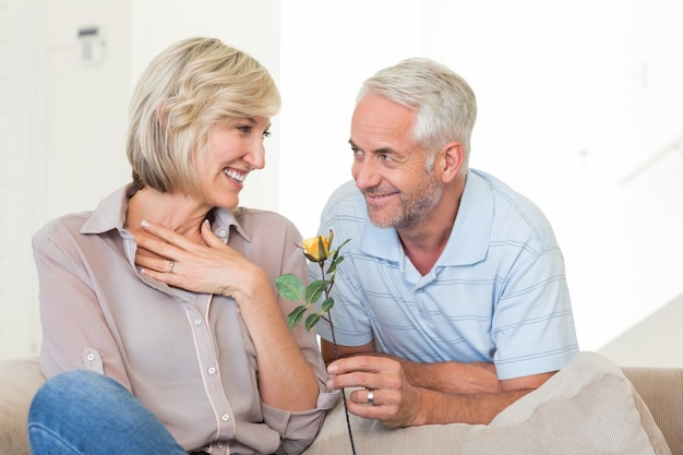 Homem dando flor a uma mulher sorridente sentada no sofá