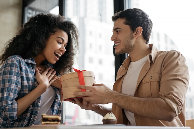 Homem dando presente de aniversário para mulher bonita. Casal multirracial sentados juntos no café, namoro