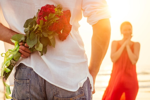 Homem dando rosas para sua surpresa e mulher maravilha na data romântica da praia do oceano ou conceito de casamento ou dia dos namorados por casal apaixonado comemorando 8 de março dia da mulher e feliz aniversário