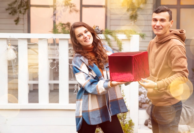 Foto homem dando um presente de natal para a namorada, eles segurando uma caixa vermelha com um presente de dia dos namorados