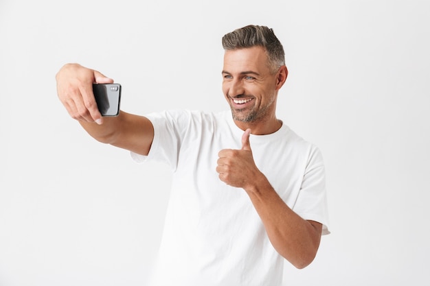 Homem de 30 anos de sucesso vestindo uma camiseta casual tirando uma selfie isolada no branco