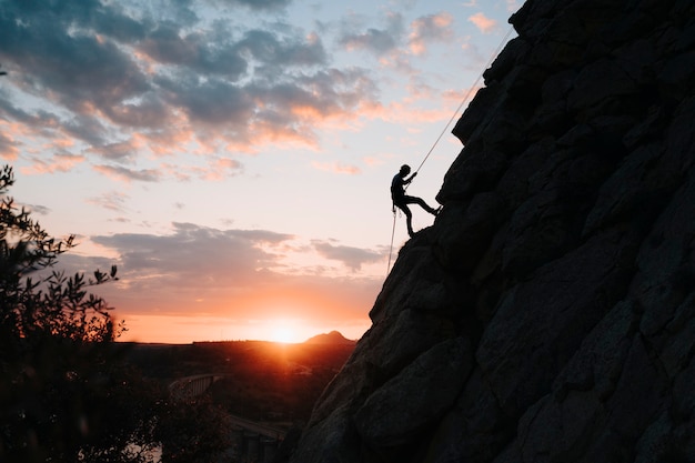 Homem de 30 anos escalando uma montanha ao pôr do sol