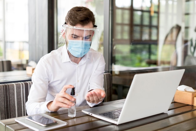 Homem de alto ângulo com máscara trabalhando no laptop