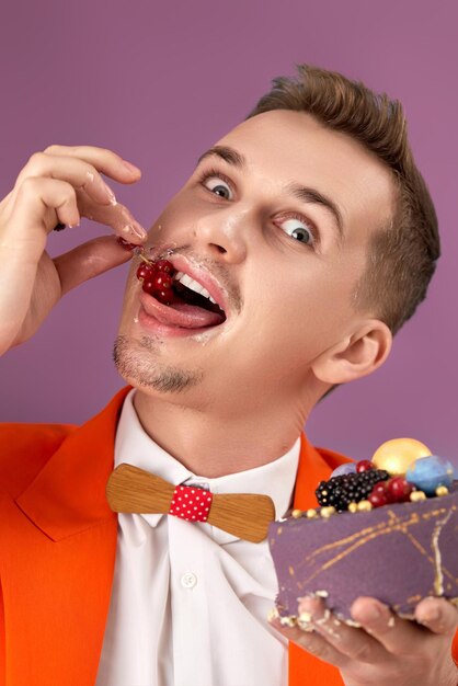 Foto homem de aniversário bonito com jaqueta laranja comendo bolo em fundo roxo