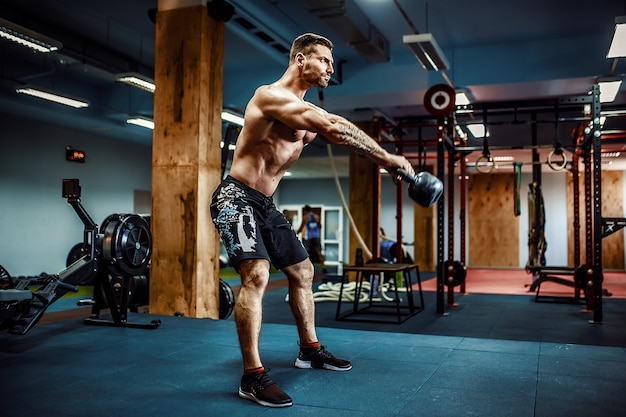 Homem de aptidão balançando kettlebells na Academia