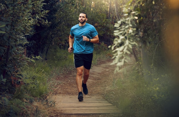 Foto homem de aptidão e correndo na natureza para treinamento de exercício saudável e treino ao ar livre corredor masculino atlético ativo em esportes fazendo uma corrida na floresta ou parque para saúde e bem-estar cardiovascular