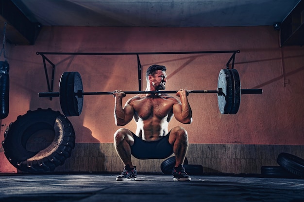 Homem de aptidão muscular empurrando uma barra sobre a cabeça em sua garagem, autoisolamento. Treino funcional. Snatch exercício.