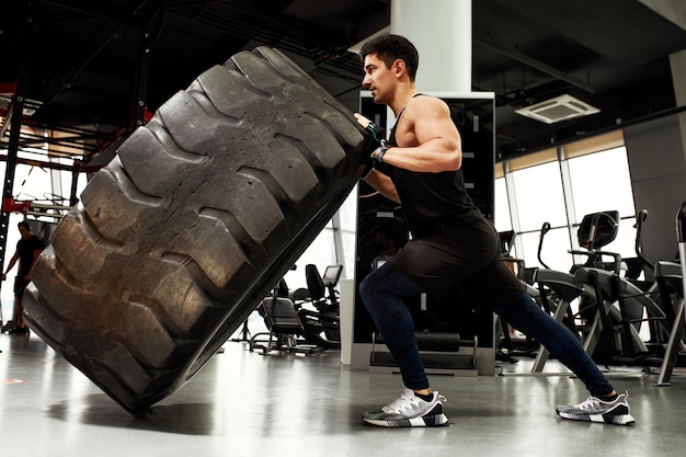 Homem de aptidão muscular movendo pneu grande no conceito de centro de ginástica levantando treinamento de treino