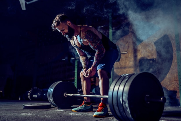 Homem de aptidão muscular, preparando-se para levantamento terra de um barbell no moderno centro de fitness. Treino funcional.