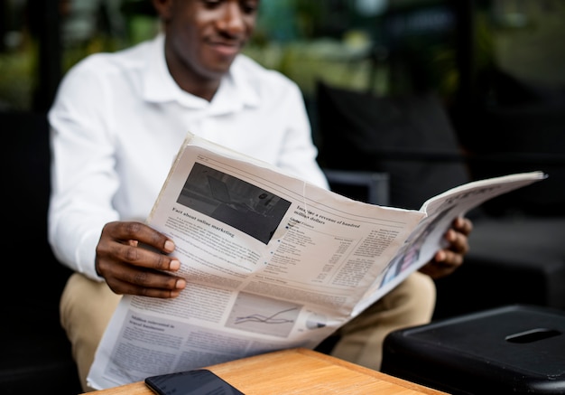 Homem de ascendência africana sentado lendo um jornal ao ar livre
