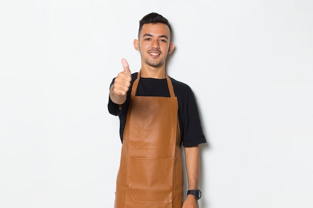 Homem de avental bonito sorrindo orgulhoso e feliz com sinal de ok tumb isolado no fundo branco