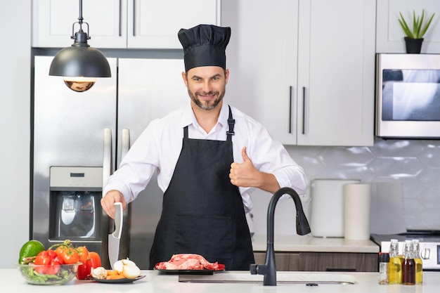 Homem de avental e chapéu de chef cozinhando comida na cozinha homem bonito cozinhando comida saudável na cozinha cara