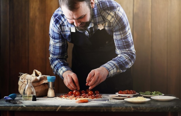 Homem de avental preparando pizza, sove a massa e coloca os ingredientes