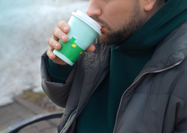 Homem de barba bebe café na rua na primavera de perto
