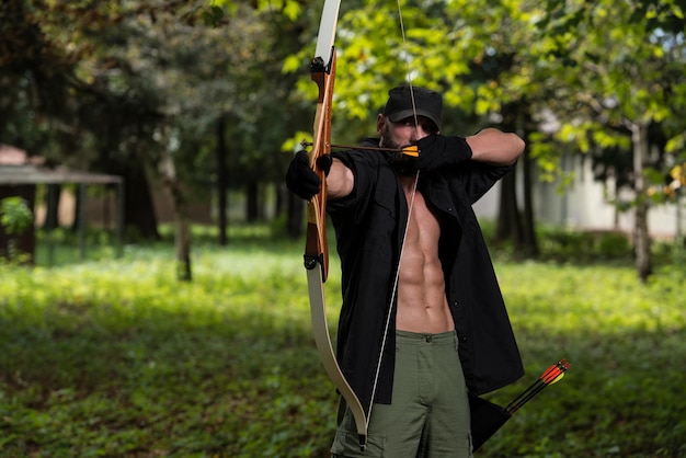 Homem de barba com um arco e flechas na floresta